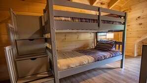 Una cama individual con cajones de almacenamiento, piso de madera y una escalera en una habitación de madera.