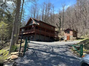A two-story log cabin with a balcony, surrounded by a forested area.