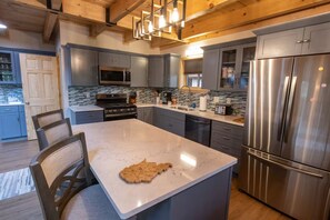A modern kitchen with a large island, stainless steel appliances, and a wooden ceiling.
