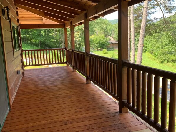 A wooden deck with a railing, overlooking a green landscape with trees.