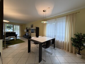 Ein modernes Wohnzimmer mit Essbereich, einer Couch, einem Couchtisch und einer Zimmerpflanze.