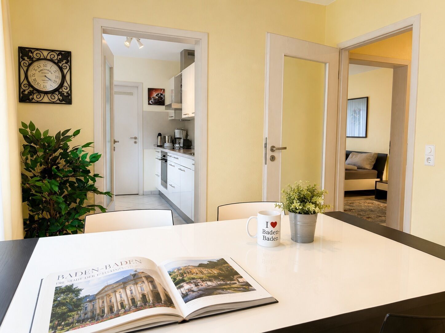 A room with a dining table, a book, a mug, and a potted plant.