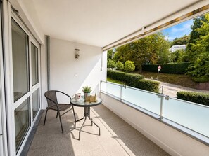 Ein Balkon mit Glastrennwand, einem Tisch und zwei Stühlen sowie einem Blumentopf.