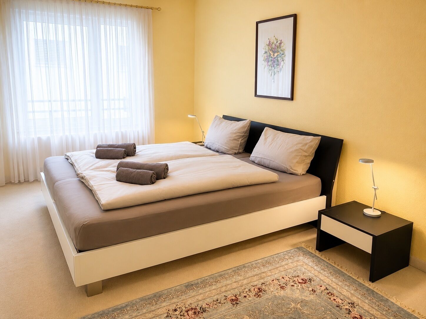 A double bed with a headboard, two bedside tables, a rug, and a framed picture on the wall.