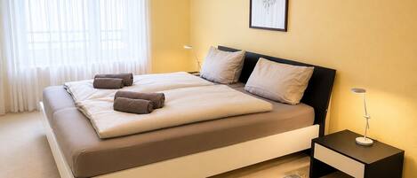 A double bed with a headboard, two bedside tables, a rug, and a framed picture on the wall.