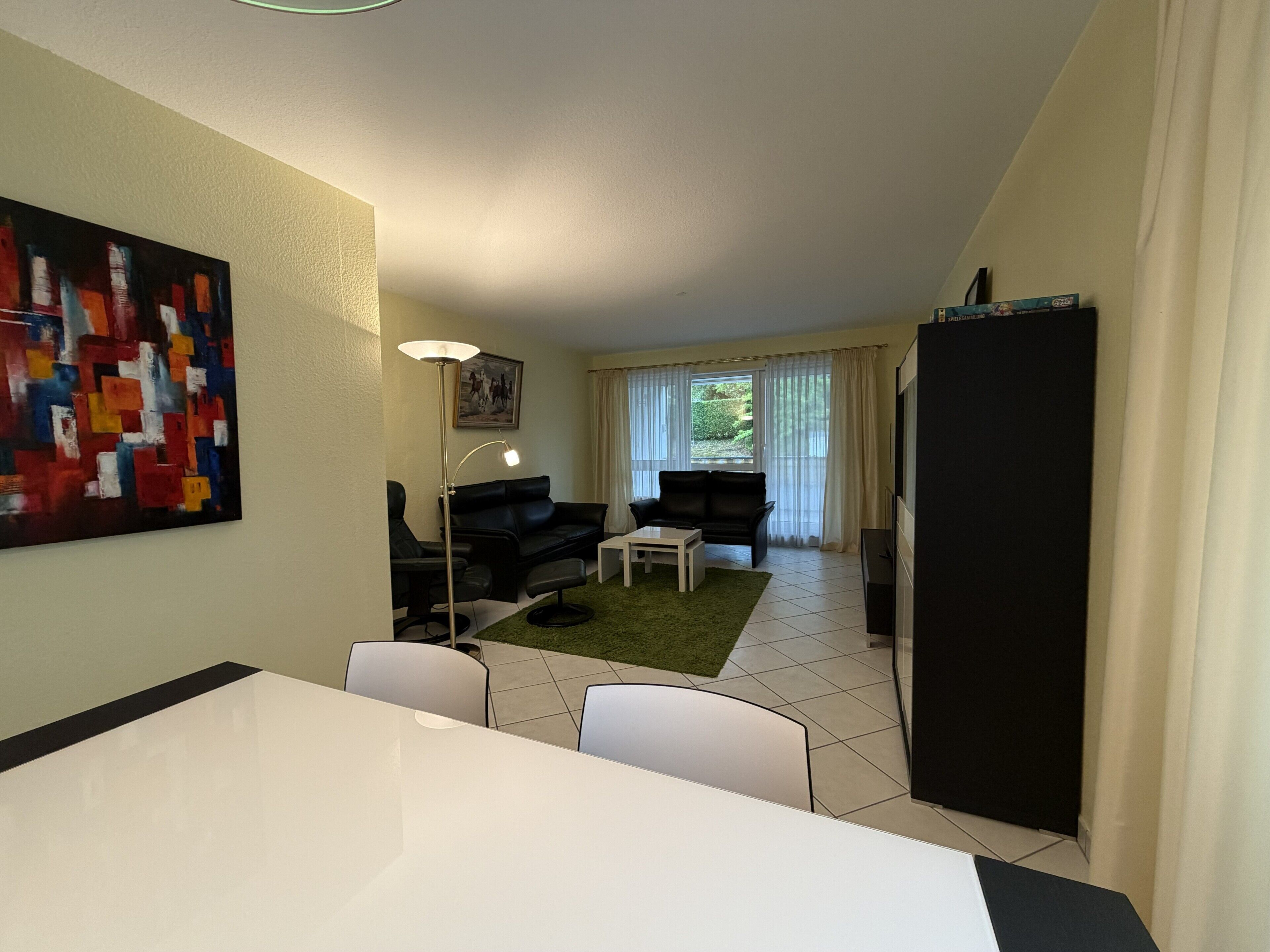 Een knus woongedeelte met een eethoek, twee zwarte banken, een klein witte tafel en een schilderij aan de muur.