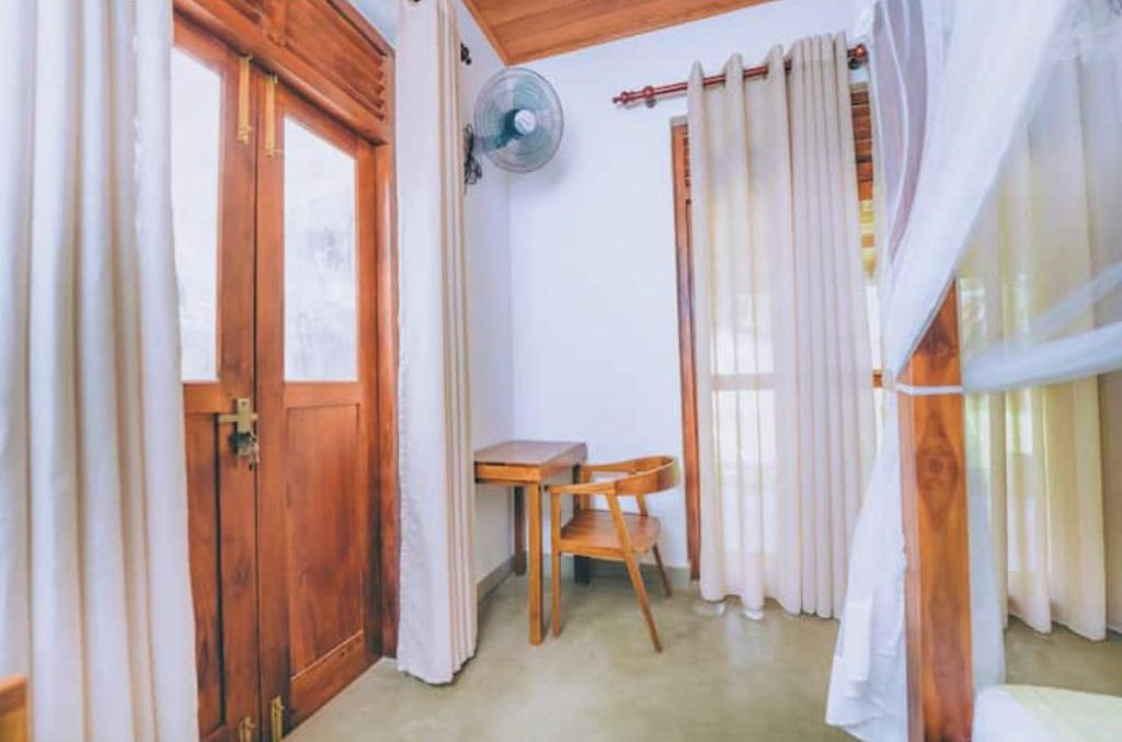 Une pièce avec une porte en bois, une petite table avec une chaise, un ventilateur et des rideaux.