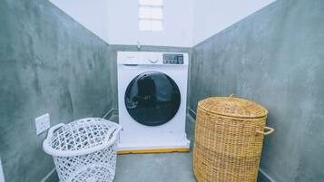 Un cuarto de lavandería con una lavadora, un cesto blanco para ropa y un cesto de mimbre.