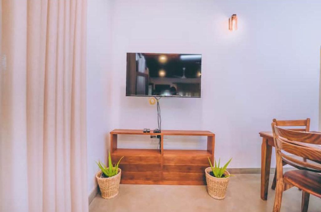 Une pièce dotée d’un téléviseur à écran plat fixé au mur, d’un banc en bois, de deux paniers en osier contenant des plantes et d’une table à manger en bois avec des chaises.