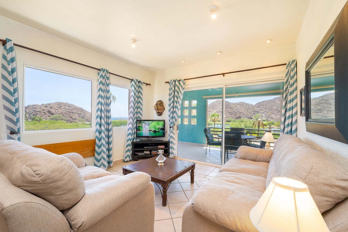 Sala de estar com televisão, sofá e vista para uma paisagem montanhosa através de uma porta de vidro deslizante.