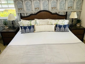 Een bed met een witte quilt, twee nachtkastjes met lampen, en een muur met een aap muurschildering.