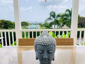 Une statue de Bouddha est posée sur une table, avec une balustrade blanche et de la verdure en arrière-plan.