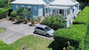 Une maison à deux étages avec un porche, entourée d’une végétation luxuriante.