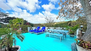 Une terrasse turquoise avec des chaises longues bleues, une table en bois et des plantes en pot.