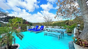 Een turquoise terras met blauwe ligstoelen, een houten tafel en pottenplanten.