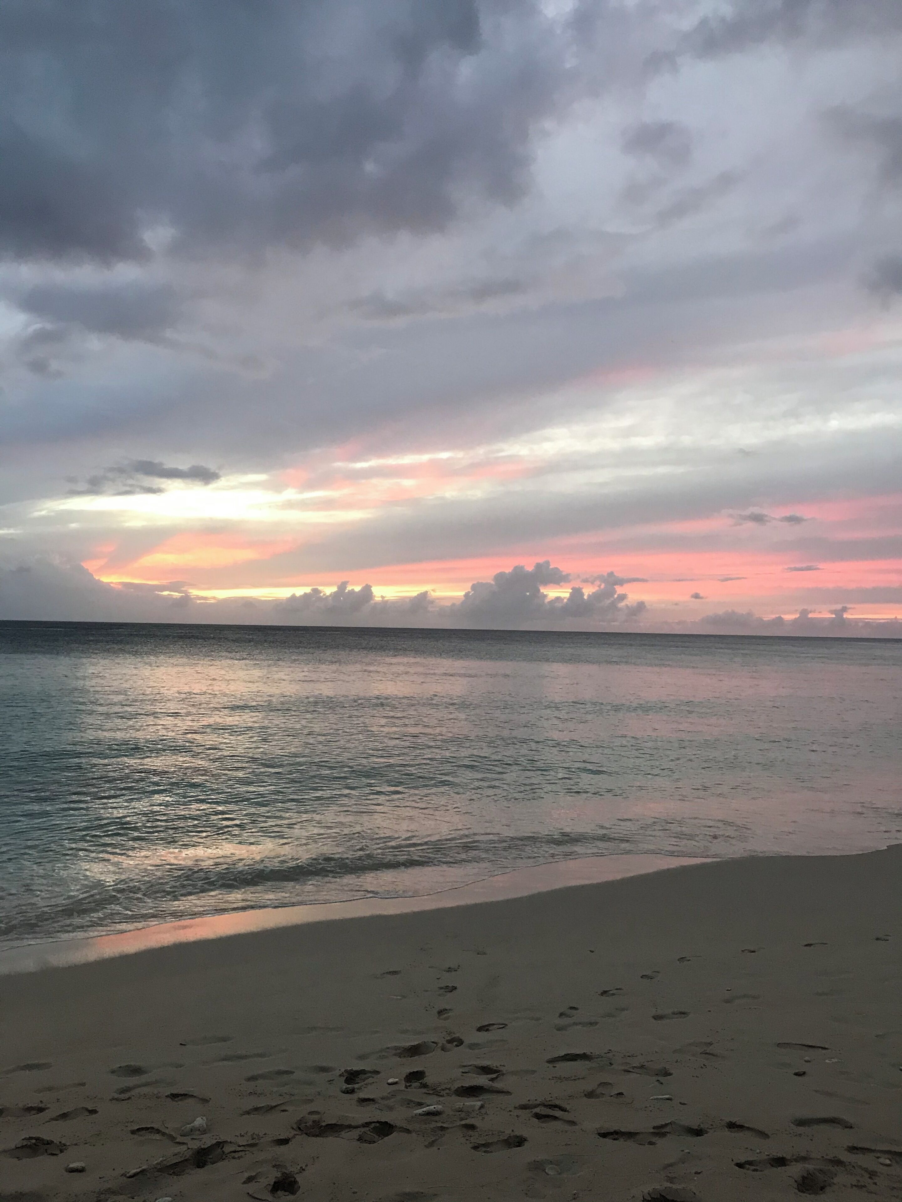 A beach with footprints leading to the water, a calm sea, and a cloudy sky.