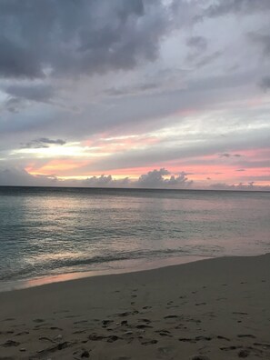 Une plage où l’on voit des empreintes de pas menant à l’eau, une mer calme et un ciel nuageux.