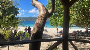 A beach scene with a wooden structure, palm trees, and people relaxing on the sand.