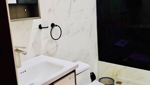 Um banheiro moderno com parede de mármore branco, pia branca, vaso sanitário e área de chuveiro.