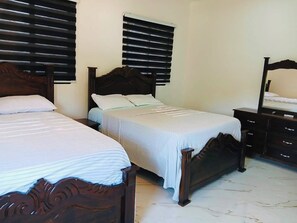 Habitación de hotel con dos camas, cabecera de madera, mesita de noche, cómoda y ventana con persianas.