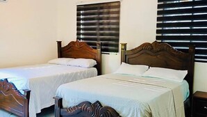 Quarto de hotel com duas camas de madeira, um ventilador de teto, janela com persianas e piso de mármore.