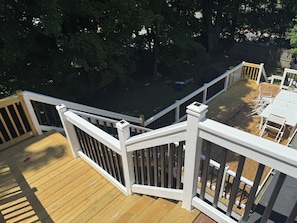 A wooden deck with white railings, surrounded by trees.