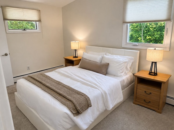 A bedroom with a bed, two bedside tables, a window with blinds, and a view of greenery outside. - Newly Renovated 1BR – 5 Minutes to Valhalla Train, White Plains, WMC & NYC (White Plains)