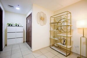 A hallway with a white wardrobe, a decorative wall clock, a gold metal shelf unit, and a floor lamp. - 3BR+Maid in JBR | Near The Walk & JBR Beach (Dubai)