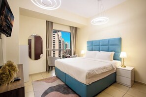 A hotel room with a large bed, a desk, a chair, a TV, and a view of tall buildings. - 3BR+Maid in JBR | Near The Walk & JBR Beach (Dubai)