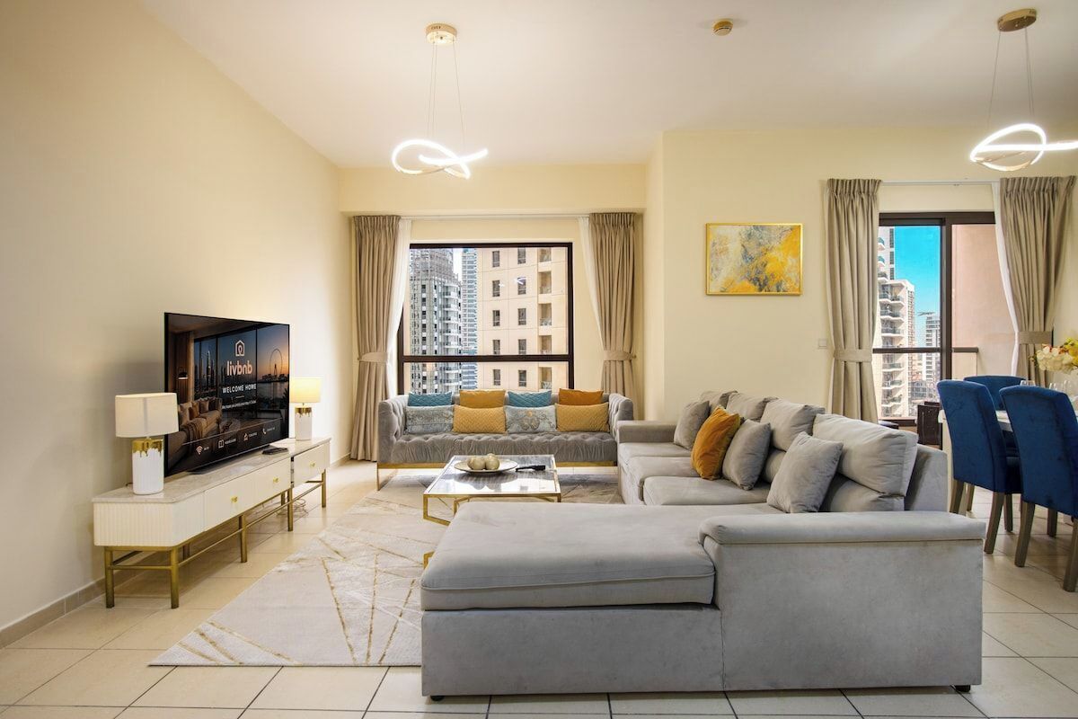Un salon moderne avec un canapé, une table basse, un téléviseur et une vue sur des immeubles de grande hauteur.
