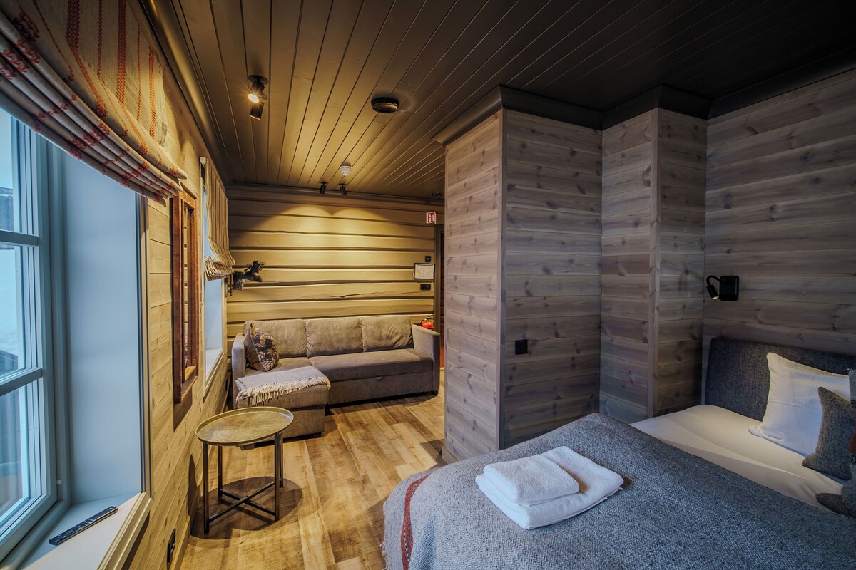 A cozy wooden cabin room with a bed, a sofa, and a small table.