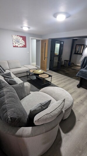 Una sala de estar con un sofá modular, una mesa de centro con placas decorativas y una puerta que da a otra habitación.