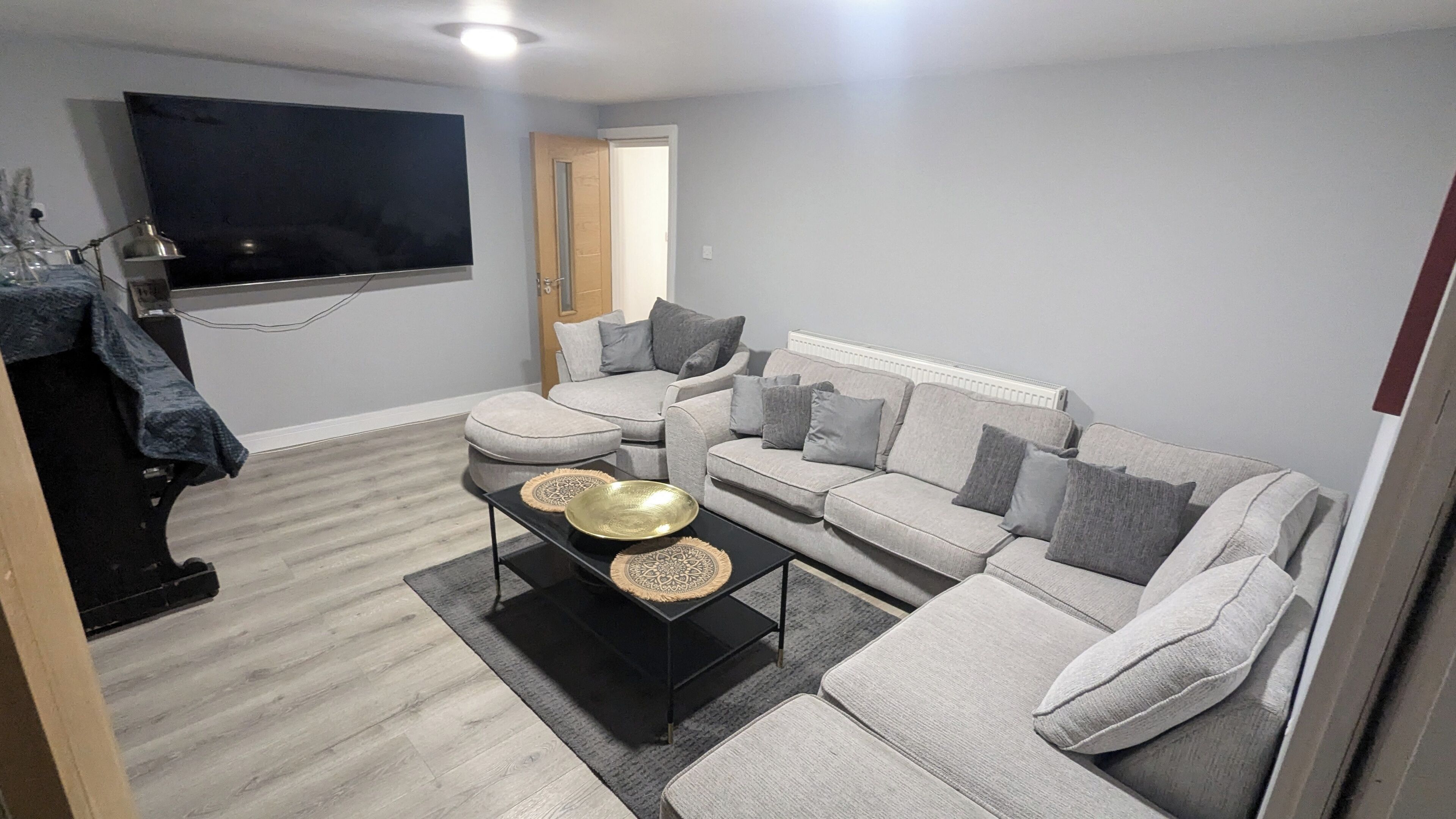 A living room with a grey sofa set, a flat-screen TV mounted on the wall, and a coffee table with decorative items.