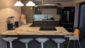 Una cocina moderna con encimera de mármol, dos luces colgantes, horno empotrado y refrigerador.