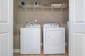 A laundry area with two white washers and dryers, a metal drying rack with boxes and an iron, and a wooden floor. - Sevierville Cabin Near Dollywood, Sleeps 6, Hot Tub (Sevierville)