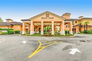A hotel named Regal Oaks with a central entrance, a driveway with directional arrows, and a landscaped area with palm trees. - Sunshine Haven Retreat (Kissimmee)