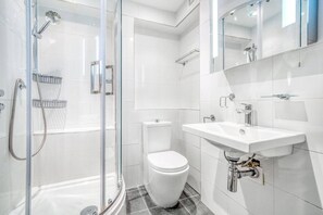 Een moderne badkamer met een douchecabine van glas, een wit toilet en een wastafel met spiegel erboven.