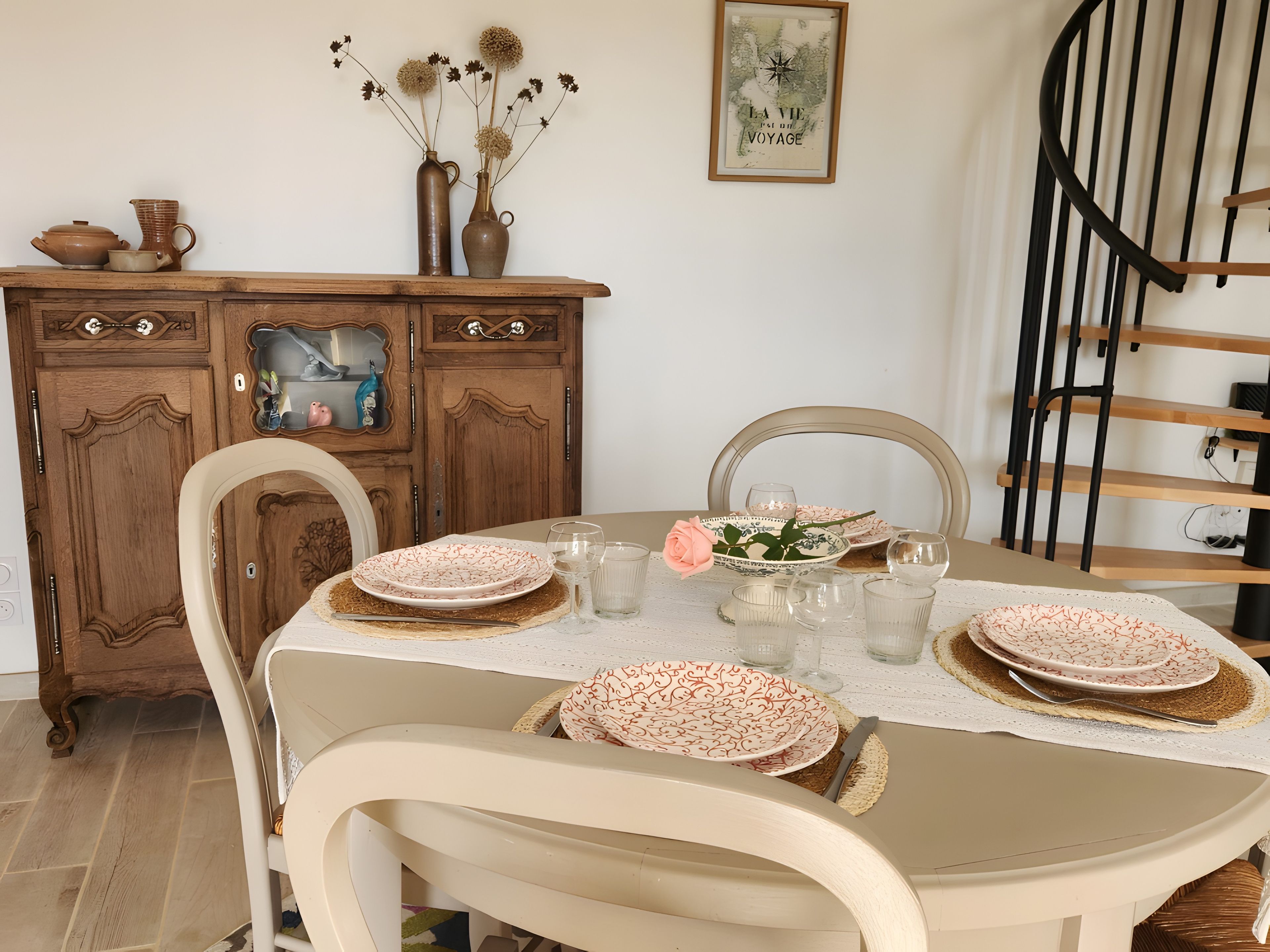 A dining table with plates, glasses, and a vase with dried flowers.