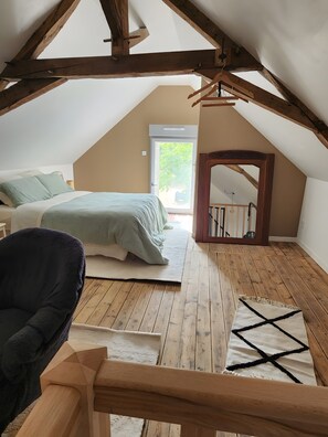 Een slaapkamer met een schuine kap, een bed, een stoel en een houten vloer.