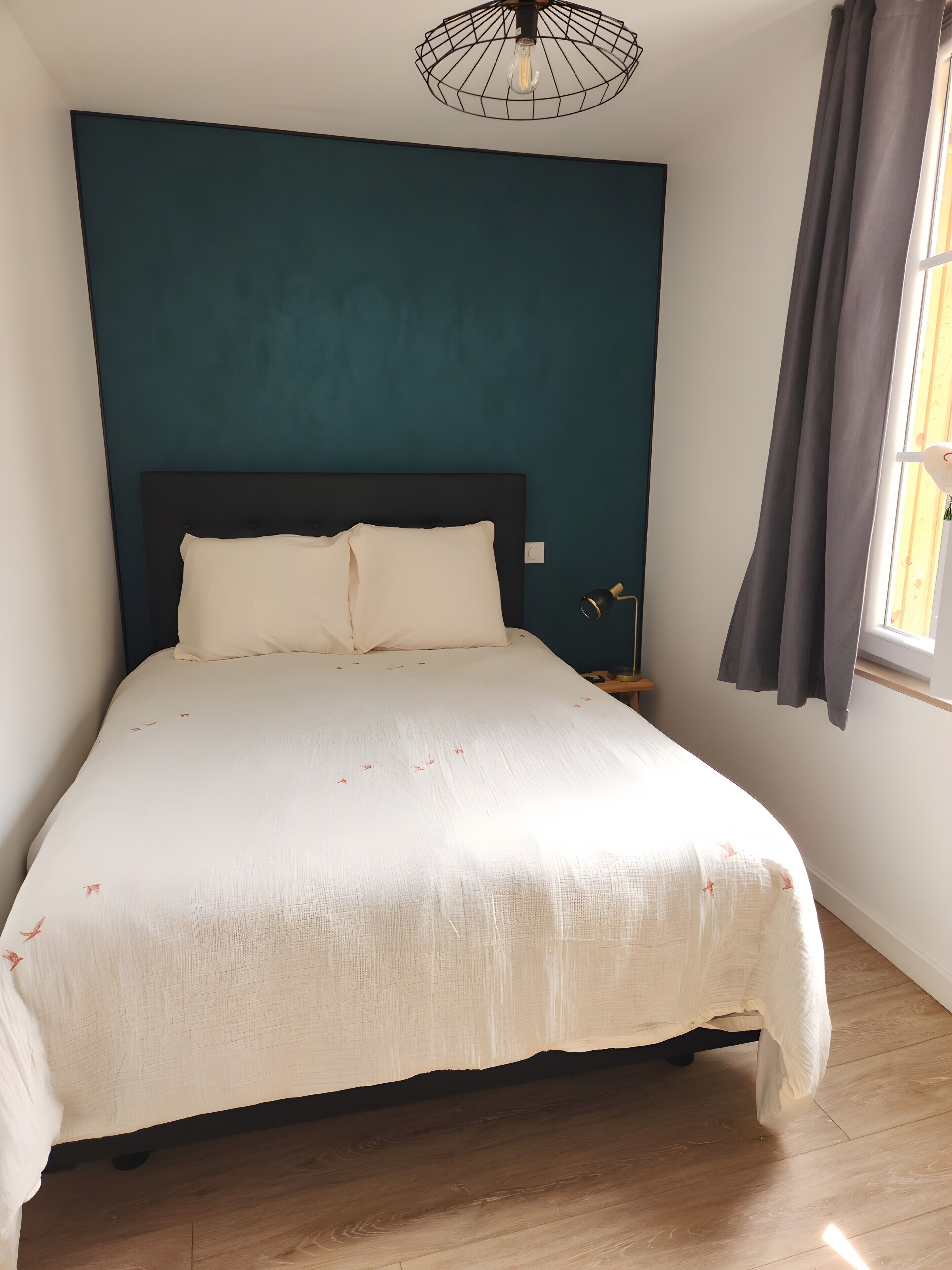 A bedroom with a bed, a nightstand, a lamp, and a window with curtains.