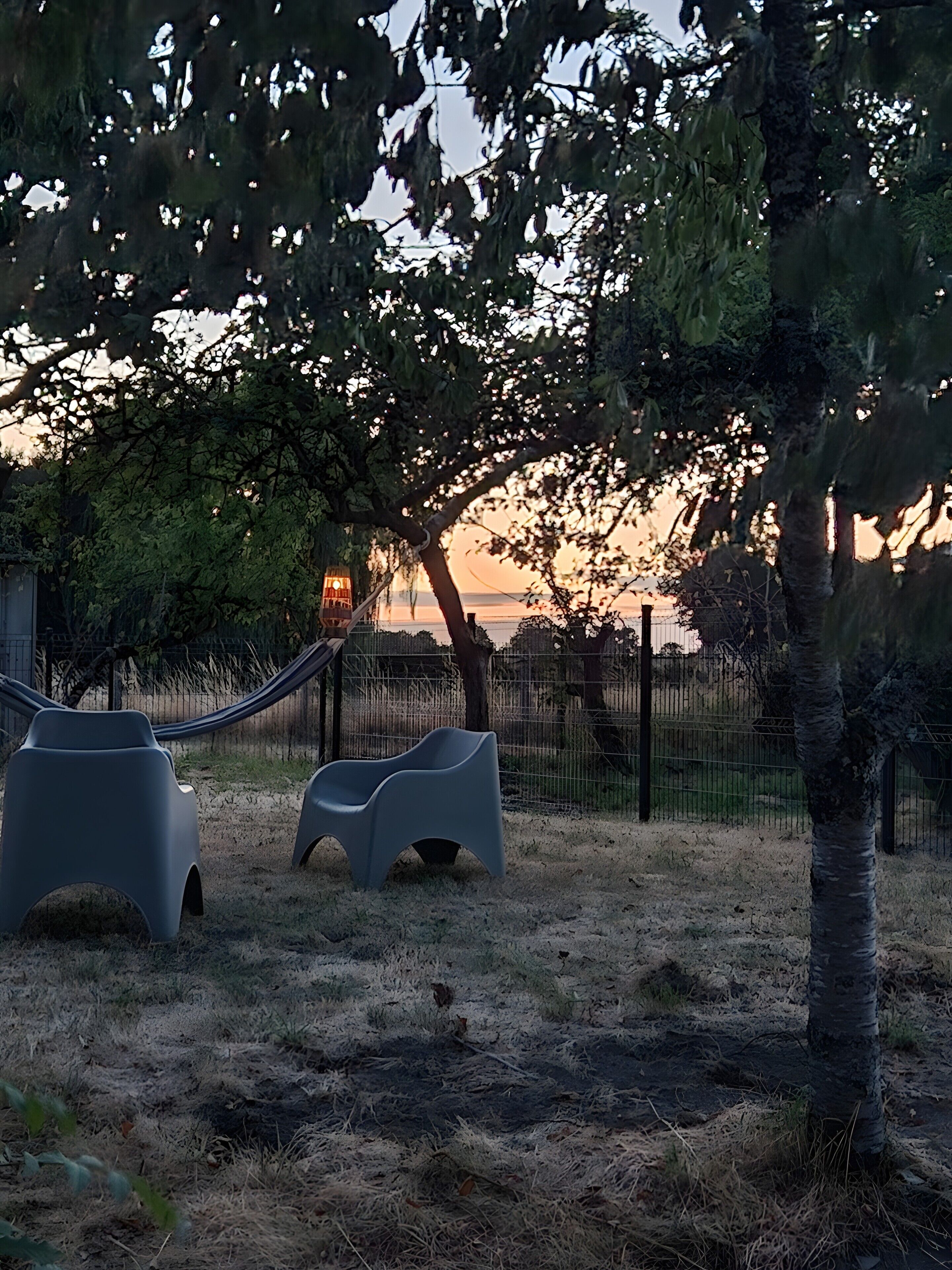 Een park met een hangmat, twee moderne stoelen en een hek.