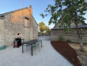 Een stenen gebouw met een terras van grind, een tafel met stoelen en een boom.
