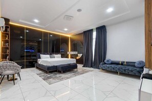 A modern bedroom with a large bed, a sofa, a chair, and a TV. - Shu Garden Hotel (Lagos)