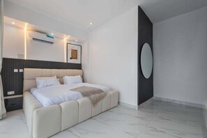 A modern bedroom with a large bed, a wall-mounted air conditioner, and a large mirror. - Shu Garden Hotel (Lagos)