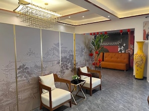 Quarto com um mural tradicional em estilo asiático, duas cadeiras de madeira, um sofá moderno e um vaso amarelo.