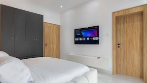 A bedroom with a bed, a TV mounted on the wall, and two doors. - Shu Garden Hotel (Lagos)