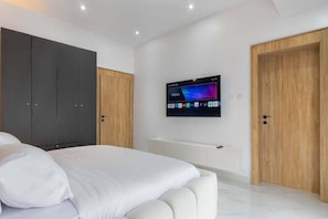 Quarto com cama, televisão na parede e duas portas.