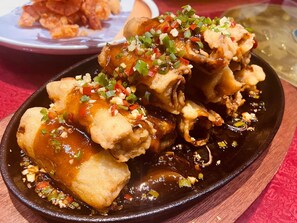A dish of fried chicken with a dark sauce and chopped green peppers on a black plate. - Shu Garden Hotel (Lagos)