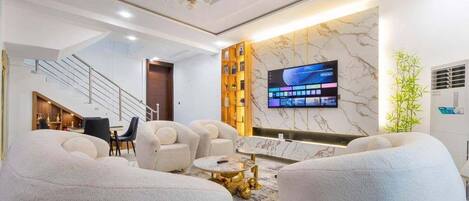 A modern living room with a flat-screen TV, plush seating, a staircase, and a decorative wall.