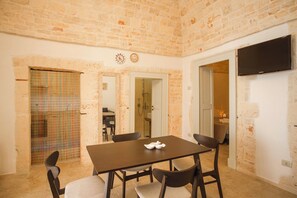A room with a brick wall, a dining table with chairs, a TV mounted on the wall, and a door leading to another room. - Stone House—A Stone House in the Heart of Alberobello (Alberobello)